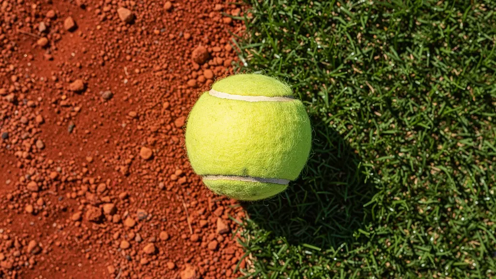 Vue macro montrant la texture de la terre battue d'un côté et du gazon de l'autre avec une balle de tennis au centre